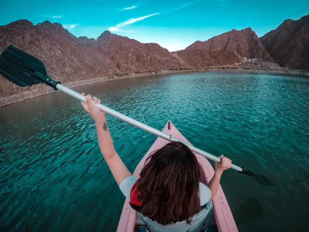 Kayaking on a calm lake surrounded by rugged mountains in Hatta, enjoying an adventure sports experience with clear blue skies and scenic natural views.
