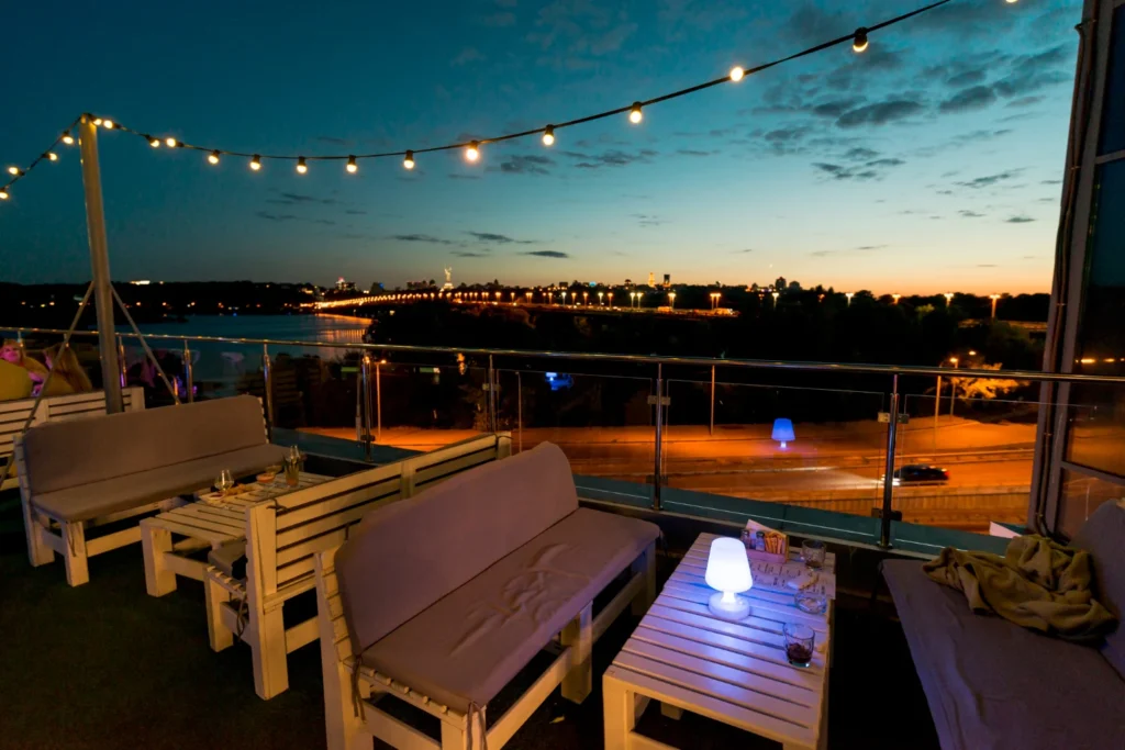 A rooftop lounge with benches, lights, and water side