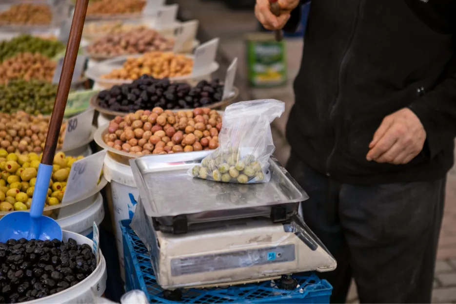 A man weighing olives on the weight machine with other types of olives