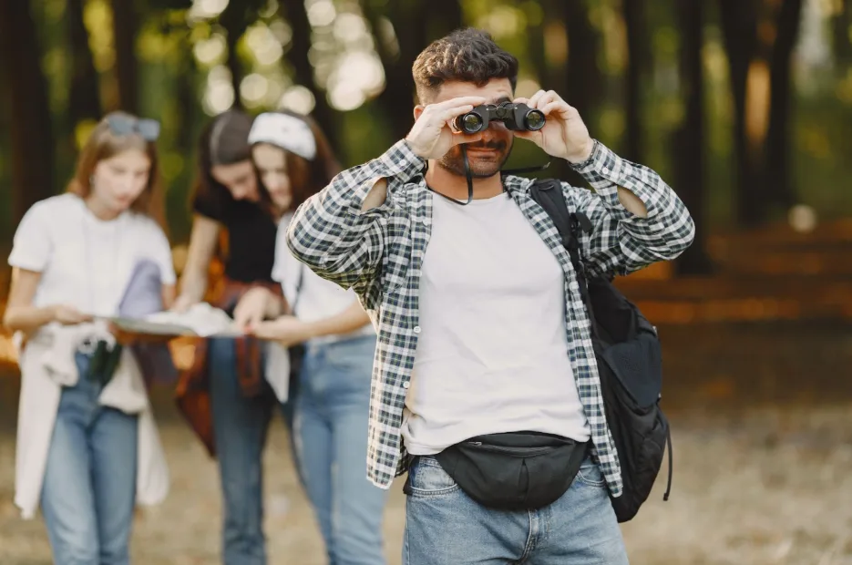 A guy watching through binoculars with three women checking the map