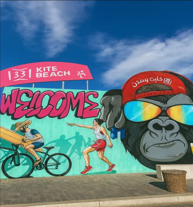 Street art at Kite Beach in Dubai with a gorilla in a red cap, “WELCOME” text, and cyclist and runner figures.