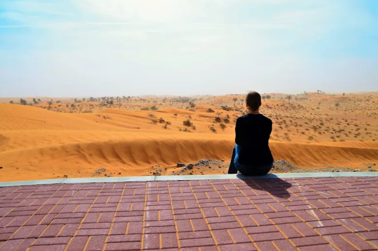 Person sitting on a tiled platform overlooking the vast desert dunes of Ras Al Khaimah, highlighting the emirate’s natural landscapes near its historic villages.