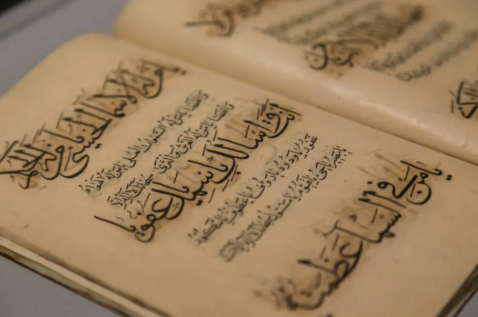 Close-up of an open antique manuscript with Arabic calligraphy in bold black ink on aged parchment pageso content