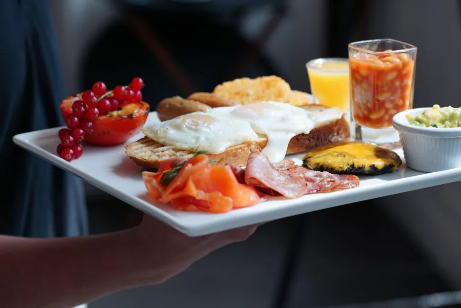 A gourmet breakfast spread on a white ceramic tray features poached eggs, smoked salmon, toast, grilled tomato, and baked beans.