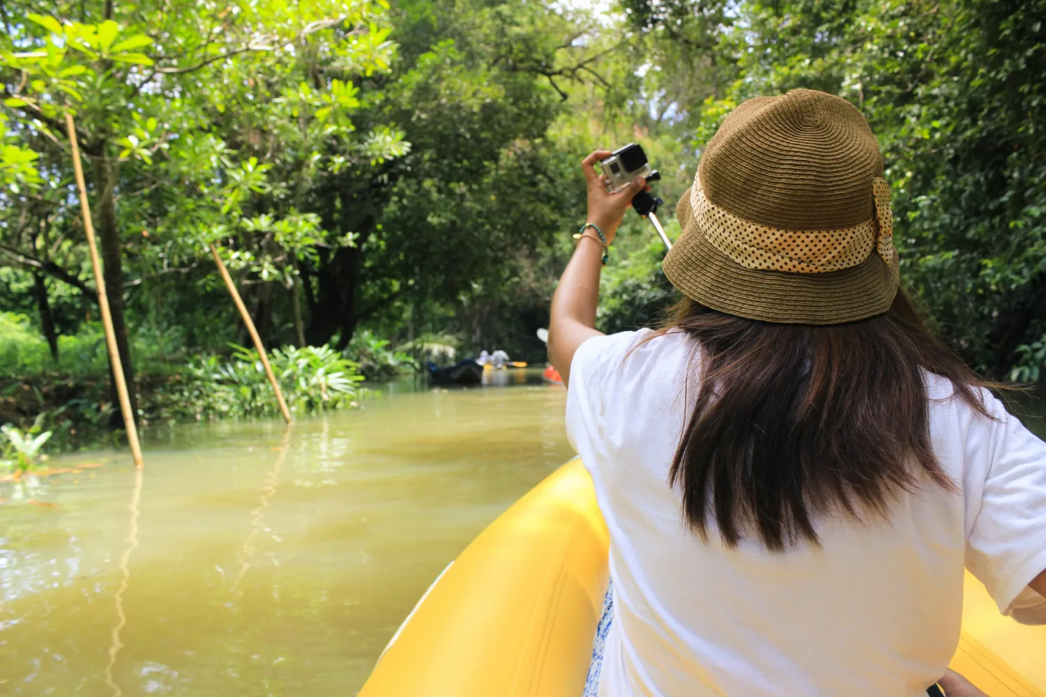 A woman with a hat kayaking in a yellow kayak 