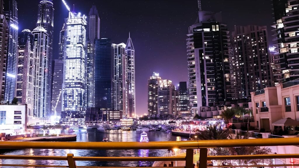 Dubai Marina at night with illuminated skyscrapers, yachts on the water, and the lively Marina Walk filled with restaurants and people.